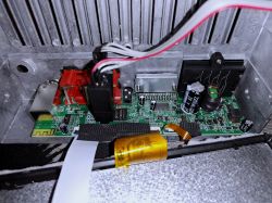 Inside a device: green PCB with connectors, wires, ribbon cables, and capacitors in a metal housing