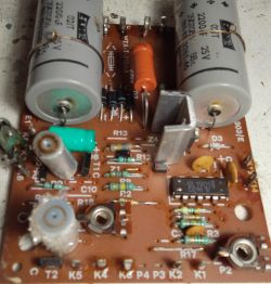 Zdjęcie płytki drukowanej z różnymi komponentami elektronicznymi, w tym dużymi kondensatorami elektrolitycznymi i oznaczonymi drogami sygnału.