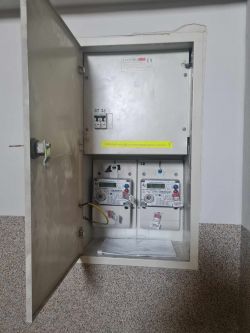 Otwarta metalowa skrzynka elektryczna z dwoma licznikami jednofazowymi wewnątrz.