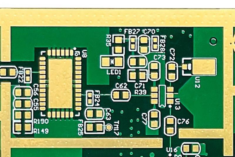 Close-up of a green PCB with electronic components marked with letters and numbers.
