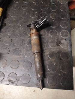 Worn fuel injector lying on a black rubber workshop mat