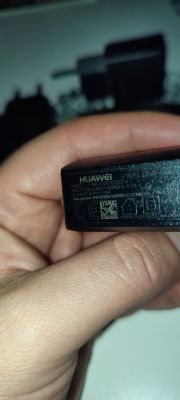 Zbliżenie na ładowarkę Huawei trzymaną w dłoni, pokazującą specyfikację techniczną na obudowie.