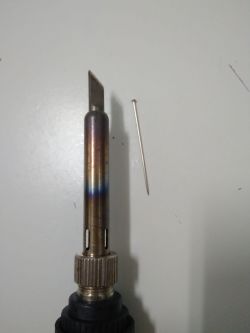 Soldering iron with heated tip next to a metal pin on a white background.