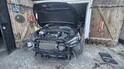 Samochód SUV z otwartą maską i zdemontowanym przednim zderzakiem stoi przed otwartym garażem, widoczne są narzędzia i akcesoria warsztatowe.