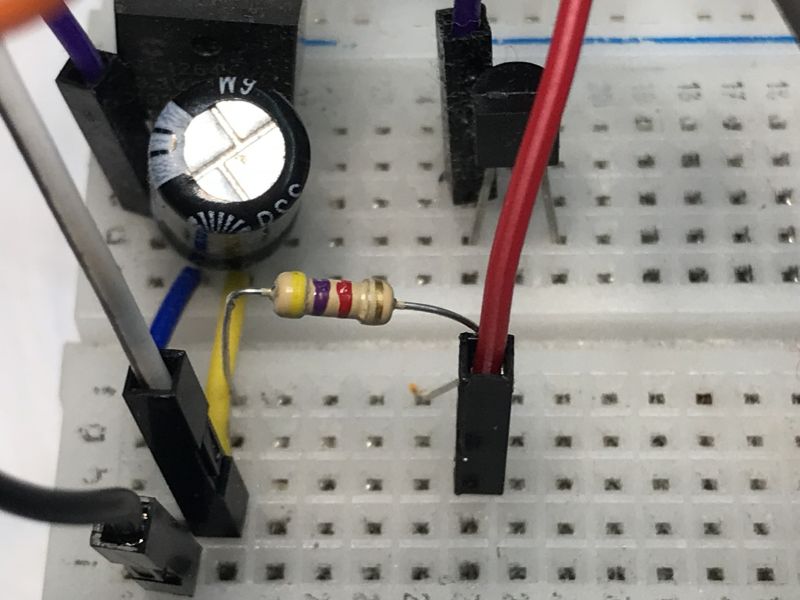 Close-up of a breadboard with a capacitor, wires, and a resistor.