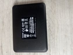 Czarny zewnętrzny dysk twardy Toshiba DTB410 1TB leży na jasnym stole, widoczna etykieta z informacjami technicznymi.
