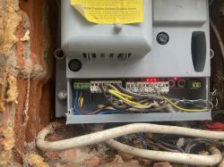 Puszka elektryczna z okablowaniem i świecącymi diodami na tle ceglanej ściany.