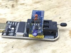 Close-up of a USB programmer with a DIP8 adapter and flash memory chip, placed on a wooden surface.
