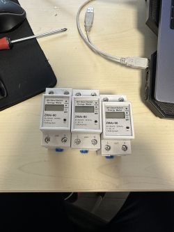 Three ZMAi-90 devices lying on a desk next to a screwdriver and a USB cable.