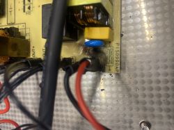 Zbliżenie na uszkodzoną płytkę elektroniczną z widocznymi kondensatorami i przewodami.