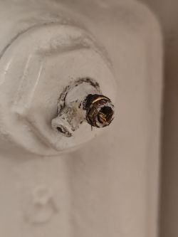 Zbliżenie uszkodzonego odpowietrznika na białym grzejniku żeliwnym