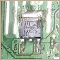 Zbliżenie na komponent elektroniczny na zielonej płytce drukowanej z trudnym do odczytania oznaczeniem.
