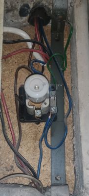 Widok na starą instalację elektryczną w skrzynce, z widocznymi przewodami i bezpiecznikiem topikowym.