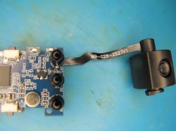 Camera module attached to PCB via ribbon cable Camera module connected via ribbon cable to blue PCB on light blue workstation