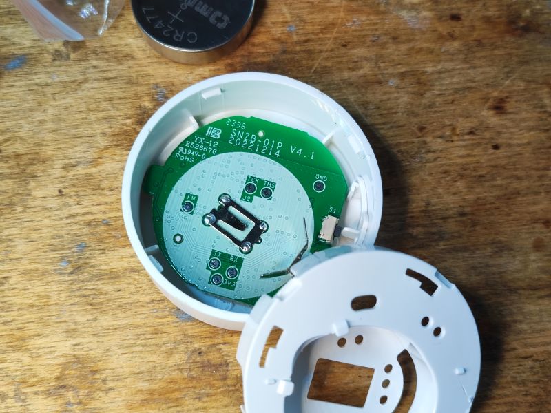 Wnętrze przycisku Sonoff SNZB-01P na tle drewnianego blatu.