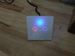 Square wall switch with two illuminated buttons on a wooden floor.