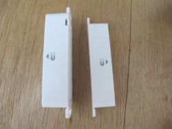 Two Sensors on a Wooden Table Two white enclosed devices on a wooden table resembling sensors.