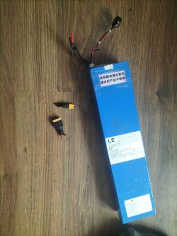 Niebieska bateria z inną wtyczką niż oryginalna leży na drewnianej podłodze.