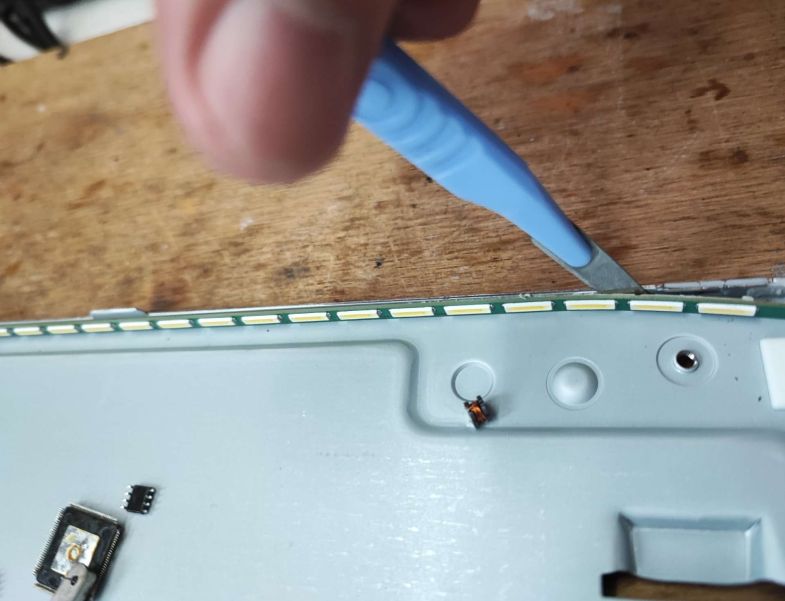 Removing LED Strip from Monitor A person is prying a LED strip from a monitor casing with a thin knife.