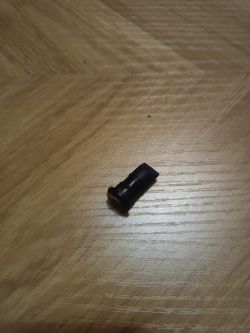 Czarny plastikowy element leży na drewnianej podłodze.