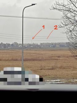 Widok na pola i zabudowania z okna; słup latarni, linie energetyczne i zaznaczone „1” i „2” na horyzoncie