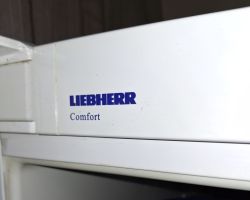 Logo „LIEBHERR” i napis „Comfort” na białym froncie lodówki, zbliżenie.