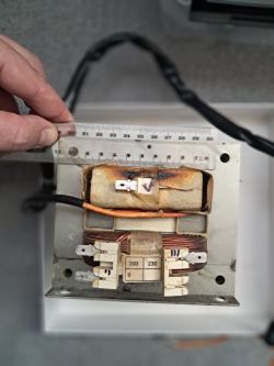 Transformator z mikrofalówki z uszkodzonym uzwojeniem wtórnym i linijką do pomiaru