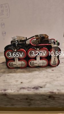 Zbliżenie na baterię DeWalt z widocznymi pomiarami napięcia ogniw: 3,65V, 3,26V, 10,58V.