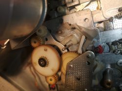 Zdjęcie wnętrza mechanizmu z kilkoma plastikowymi zębatkami i metalowymi elementami.
