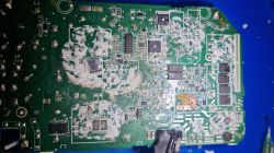 Uszkodzona płytka drukowana z elementami elektronicznymi i śladami białego nalotu.