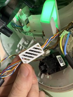 Dłoń trzyma biały, ażurowy wydruk 3D z elektroniką obok wiązek przewodów i świecącego na zielono modułu