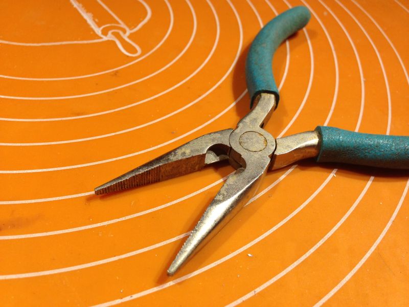 Zardzewiałe kombinerki z niebieskimi uchwytami leżące na pomarańczowej macie.