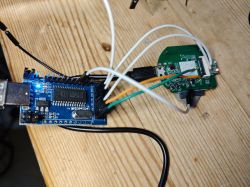 A USB programmer connected by wires to a PCB with electronics on a wooden table.