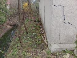 Ściana garażu z widocznymi pęknięciami i sąsiadującym rowem.