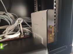 Router lub modem z zielonymi diodami w szafie rack obok splątanych kabli sieciowych