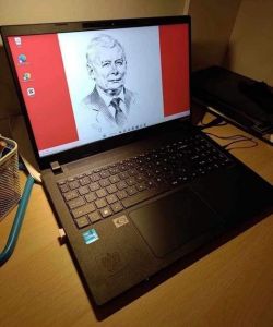 Laptop z wizerunkiem starszego mężczyzny na ekranie, stojący na biurku.