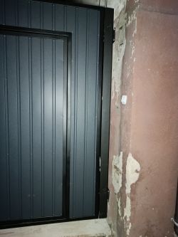 Zbliżenie na ciemnoszarą, metalową bramę zamontowaną tuż przy ścianie budynku