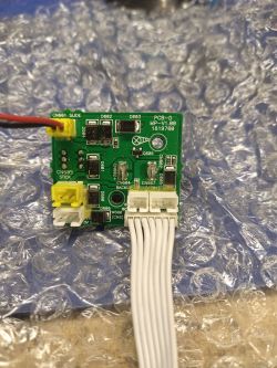 Zielona płytka drukowana z przymocowanymi komponentami elektronicznymi i białym przewodem w plastikowym złączu na tle folii bąbelkowej.