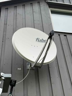 Biała antena satelitarna Fuba zamontowana na szarej elewacji budynku