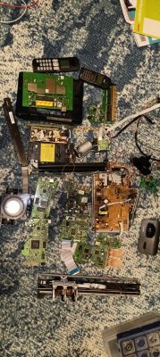 Rozłożone części elektroniki i PCB na niebieskim dywanie, m.in. płytki, silniki i elementy z drukarki.