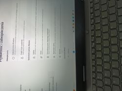 Ekran „Prywatność i zabezpieczenia” w Windows na laptopie, obok widoczna klawiatura.