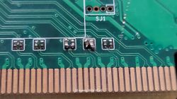 Zbliżenie płytki PCB z polami stykowymi złącza i dwoma przylutowanymi elementami SMD obok napisu „SJ1”.