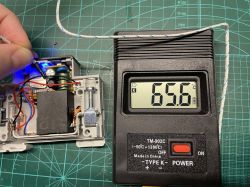 A thermometer showing 65.6°C next to an open casing with electronic components.