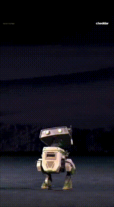 Robot tańczący na scenie, przypominający postać z animacji, z napisem cheddar w rogu