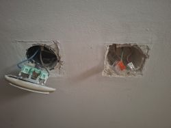 Widok na dwa otwory w ścianie z widoczną instalacją elektryczną, po lewej wyłącznik schodowy, po prawej złączki przewodów.