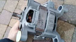 Silnik elektryczny z widocznym uzwojeniem miedzianym trzymany w ręce na tle kostki brukowej.