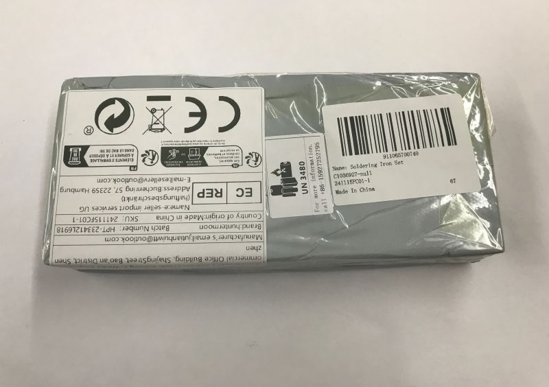 Gray plastic-wrapped box with label and barcode reading “Soldering Iron Set” on a white surface