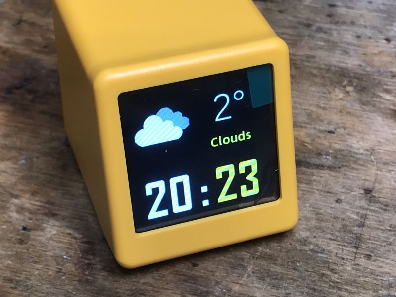Elektronisches Gadget SmallTV-Ultra mit Display Gelbes elektronisches Gadget mit Display zeigt Wolken, Temperatur 2°C und Zeit 20:23.