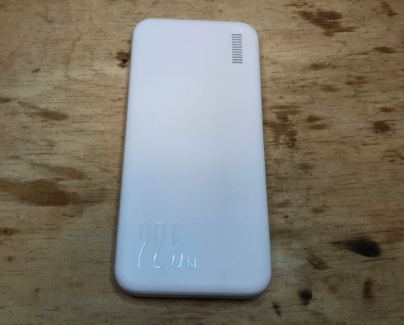 Biały powerbank leży na drewnianym stole.