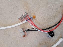 Przewody elektryczne połączone za pomocą złączek, obok wyłącznik dotykowy LED z symbolem włącznika, leżące na jasnej powierzchni.